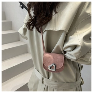 Pink heart-lock mini crossbody bag detail shown on a model wearing a beige trench coat