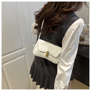 Detail shot of a beige patent leather shoulder bag with gold metal buckle on a model
