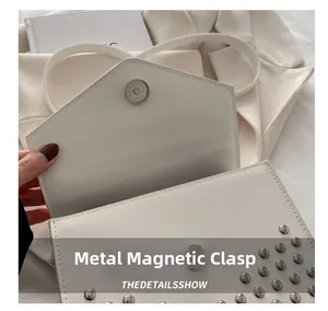 Detail of white leather crossbody bag showing the magnetic snap closure and silver studs