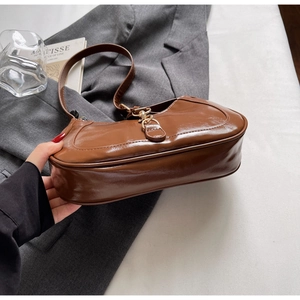 Gros plan d'un sac porté épaule en cuir synthétique marron brillant et boucle dorée