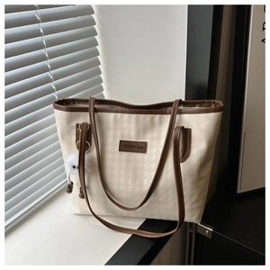 Detail of a beige tote bag with brown leather trim and a white plush keychain
