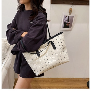 Detail of white embossed tote bag with black bow print and leather shoulder straps
