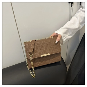 Detail of dark brown woven textured leather handbag with gold metal bar and chain strap
