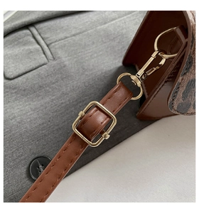 Détail de bandoulière réglable en cuir marron avec boucle dorée et motif léopard