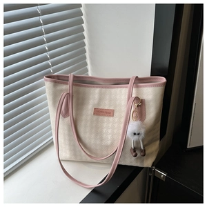 Detail of cream houndstooth tote bag with pink leather trim and white plush charm