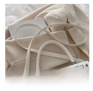 Close-up of white crossbody bag showing silver rivets, leather strap and round handle
