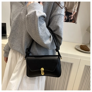 Detailed view of black leather shoulder bag with gold buckle and knotted strap on model