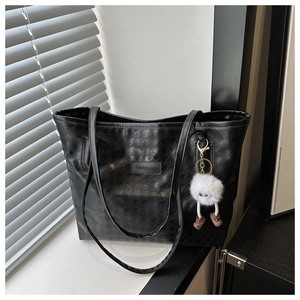 Detail of black houndstooth embossed tote bag with leather tag and white fur charm decoration
