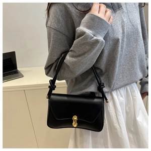 Detail of a chic black underarm bag with a gold metal clasp and knotted shoulder strap