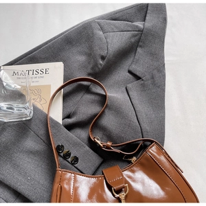 Détail du sac sous le bras marron brillant avec boucle dorée sur un blazer gris