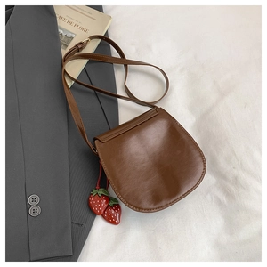 Dettaglio di una borsa a tracolla vintage marrone scuro con ciondoli a fragola rossi