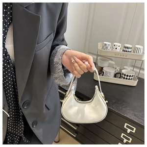 Close-up of a white minimalist crescent handbag with gold hardware and leather texture