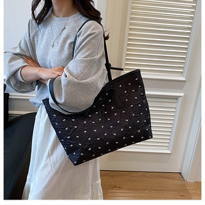 Detailed side view of large black tote bag with white bow pattern on a female model