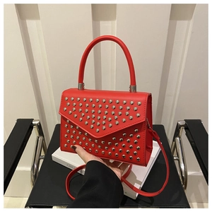 Detail of red crossbody bag with silver stud accents held by hand against a minimal background