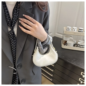 Detailed close-up of a white leather crescent handbag with elegant gold zipper and handle