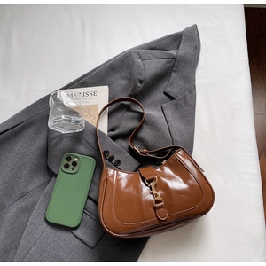 Détail d'un sac sous le bras brillant caramel avec boucle en métal sur fond de blazer gris