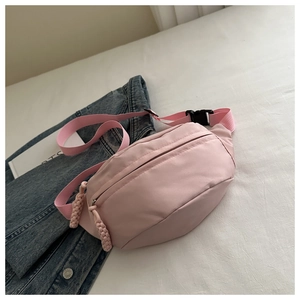 Detail of light pink nylon belt bag with woven zipper pull on a white sheet