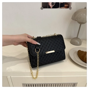 Detail of black woven texture on mini square bag with elegant gold metal clasp and chain
