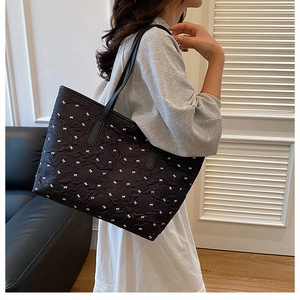 Detail of black tote bag featuring white bow embroidery and pleated texture on shoulder