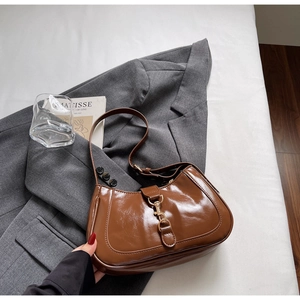 Gros plan d'un sac hobo marron brillant avec fermoir à piston doré sur une veste grise