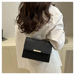 Detail of black woven texture handbag with golden chain strap on a female model