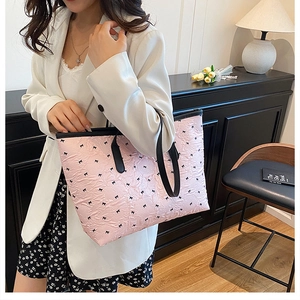 Detailed texture of pink pleated tote bag with black bow patterns and leather strap