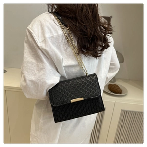 Detail of black woven texture crossbody bag with gold chain strap and metal clasp