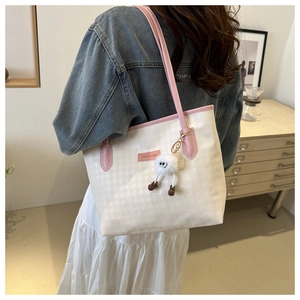 Detail of cream houndstooth tote bag with pink trim and cute plush charm on a model
