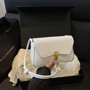 Minimalist white shoulder bag with gold clasp and textured strap on silk cushion
