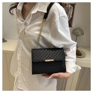 Detail of black woven texture handbag with gold chain strap and metallic buckle