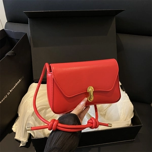 Elegant red leather shoulder bag with gold buckle and knot strap on white silk background
