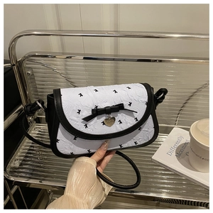 Détail d'un sac à bandoulière blanc texturé avec nœud noir et pendentif cœur