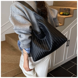 Detail view of black woven leather tote bag with Intrecciato pattern on model shoulder