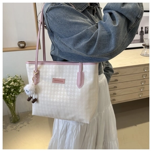 Detail of a large houndstooth tote bag with pink leather handles and a plush charm