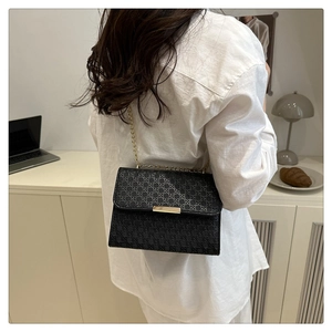 Detail of a black woven leather bag with gold chain strap worn by a model in a modern room