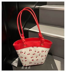 Detail of red cherry print tote bag with contrasting red handles on a minimalist background