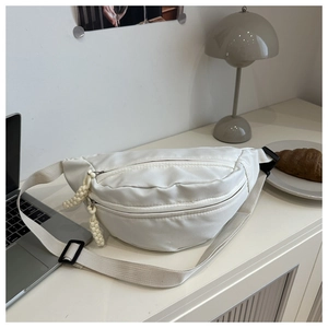 Close-up of white nylon crossbody bag with dual zip pockets and woven pullers on a desk