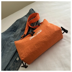 Detailed shot of orange nylon crossbody bag with textured fabric and white lettering