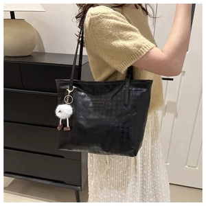 Close-up of black leather tote bag featuring white plush charm and fashion text detail
