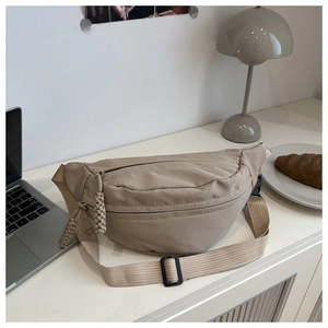 Detail of khaki nylon chest bag with woven zipper pull on a lifestyle desk setting