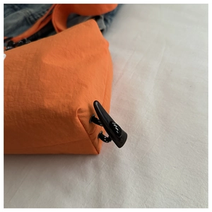 Detail view of orange nylon bag featuring black horn toggle and woven drawstring cord