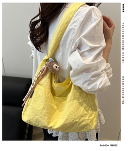 Close-up of bright yellow nylon shoulder bag featuring pleated texture and cute charms