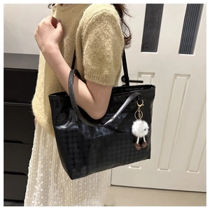 Detail of black large capacity tote bag with houndstooth texture and white fur ball charm