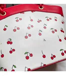 Close-up of white bucket bag featuring red cherry print and red leather handle detail