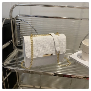 Close-up of white woven texture bag with gold chain strap on a glass shelf