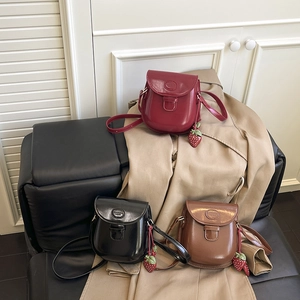 Three vintage leather saddle bags in red, black, and brown with strawberry pendants