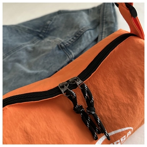 Detail of bright orange nylon crossbody bag with black dual zippers and woven pull cords