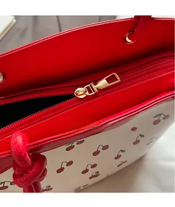 Macro detail of red cherry print bag featuring a gold zipper and smooth metal hardware