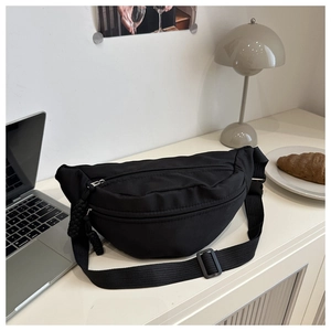 Detail of black canvas chest bag with dual zippers and adjustable buckle on white desk
