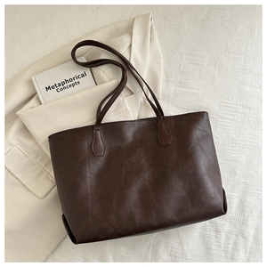 Flat lay of a dark brown large leather tote bag placed on a cream blazer and white fabric